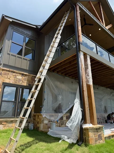 Two-story home with new gutter installation, stone veneer base, protective plastic sheeting on exterior