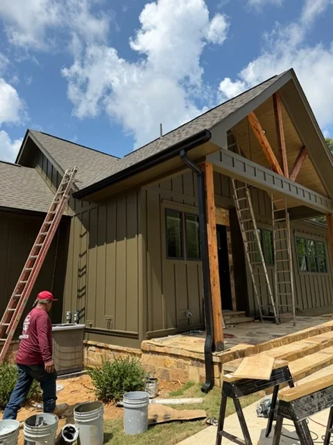 New home construction with vertical siding and gutter installation setup, ladders and materials visible