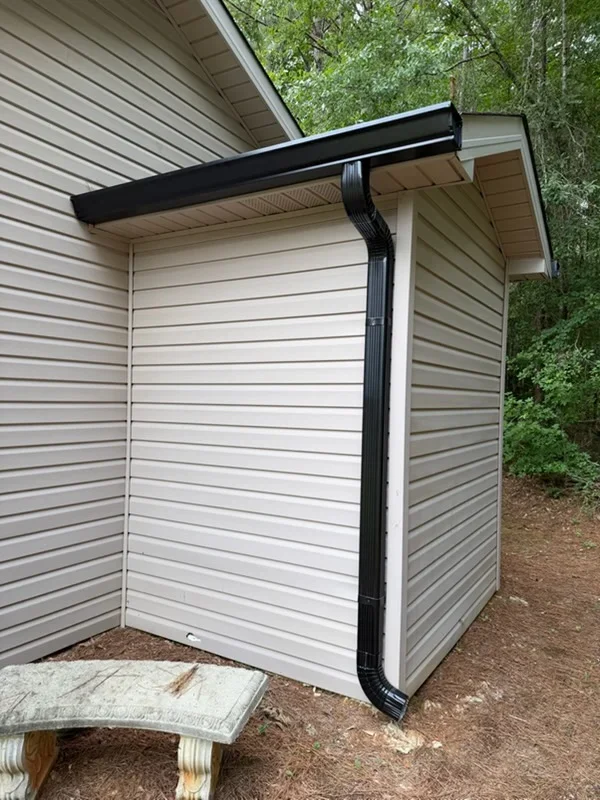 Black aluminum gutter with downspout on white metal siding structure