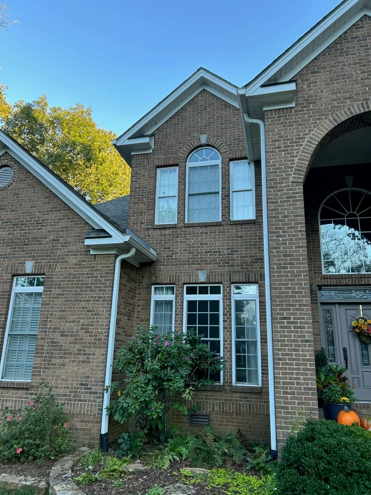 White seamless gutters and downspouts installed on brick home with gabled roofline