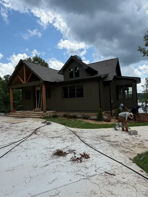 Dark siding farmhouse with gutter installation, timber accents, and multi-pitched roofline under construction